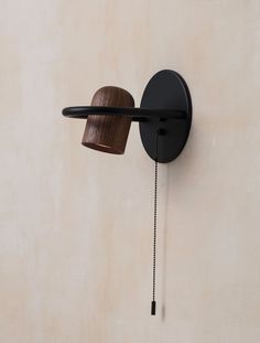 a black wall mounted light with a wooden object on it's side and a chain hanging from the arm