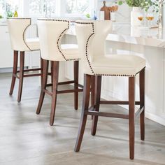 a kitchen with white counter tops and wooden barstools in front of a window