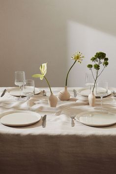 the table is set with white plates and flowers in vases on top of them