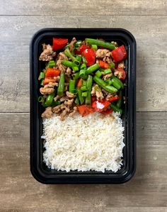 a container filled with rice, meat and veggies on top of a wooden table