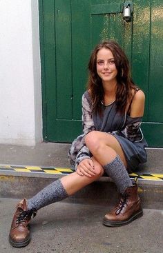 a woman sitting on the ground in front of a green door with her legs crossed