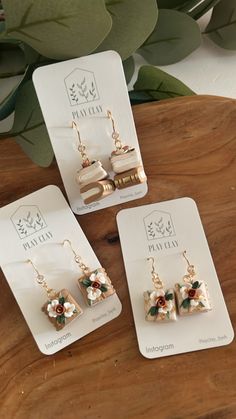 three pieces of jewelry sitting on top of a wooden table next to a plant with green leaves