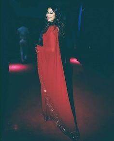 a woman in a long red dress standing on a stage with her arms around her body