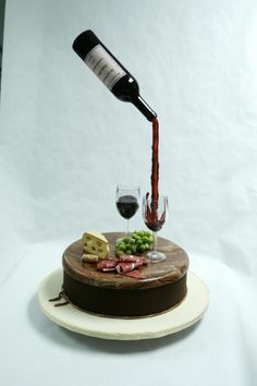 a bottle of wine being poured into a chocolate cake with cheese and grapes on it