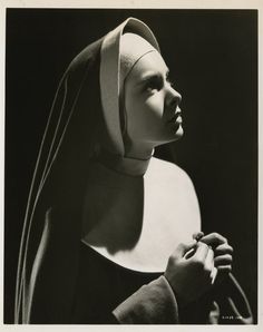 black and white photograph of woman in nun outfit with hands on her chest, looking off to the side