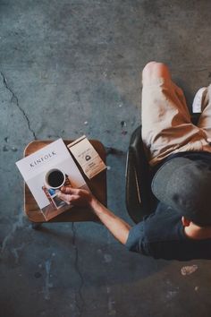 a person sitting at a table with a coffee cup and book in their hand, looking down on the floor