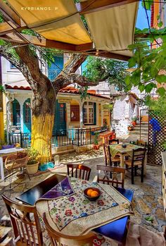 an outdoor dining area with tables, chairs and umbrellas on the outside patio in front of a tree