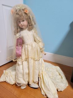 a doll dressed up in a white dress and veil with a pink purse on the floor