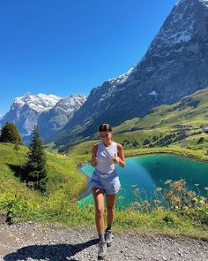 a woman running on a trail in the mountains with a lake and mountain range behind her