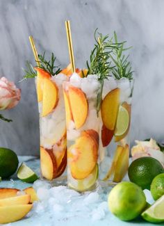 two tall glasses filled with lemonade and limes next to some sliced oranges