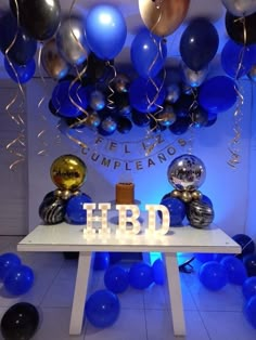 a table topped with blue and silver balloons next to a sign that says h b d