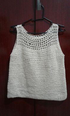 a white crocheted top hanging on a wooden door