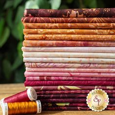 a stack of different colored fabrics sitting on top of a wooden table next to a spool of thread