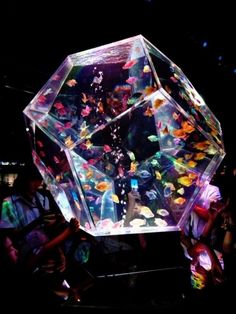 a large glass object with lots of colorful fish in it's center surrounded by people