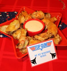 a plate with wings and dipping sauce in it on a red tableclothed table cloth