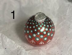 a red ornament with white and blue dots on it sitting on some paper