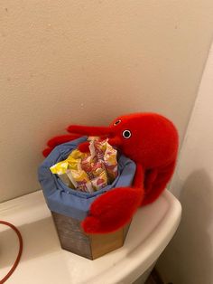 a red stuffed animal sitting on top of a toilet next to a pile of candy