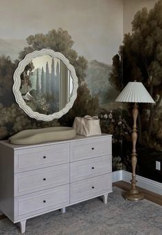 a baby crib in front of a wall with a painting on it and a lamp next to it