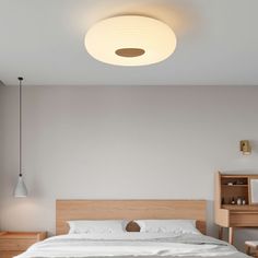 a white bed sitting under a light next to a wooden dresser and lamp on the wall