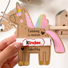 a hand holding up a candy bar with a unicorn on it's back and the word kinder written in german