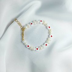 a white bracelet with red hearts and a gold charm on top of a white cloth