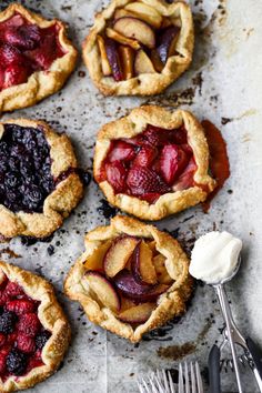 four pies with fresh fruit and ice cream on a baking sheet next to a fork