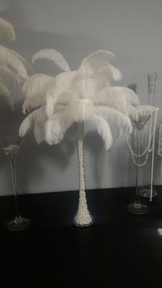 three tall vases filled with white feathers on top of a black table next to a wall