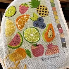 a close up of a cross stitch pattern on a table cloth with fruits and vegetables