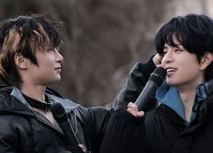 two young men standing next to each other with microphones in their hands and one holding something up to his ear