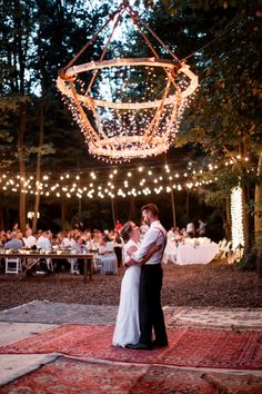 a bride and groom sharing their first dance under string lights in the woods at night