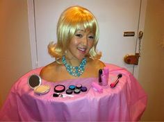 a woman with blonde hair is sitting at a table covered in makeup and other items