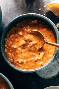 a bowl of soup with a spoon in it next to two bowls filled with food