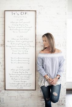 a woman leaning against a brick wall next to a sign that says it's ok