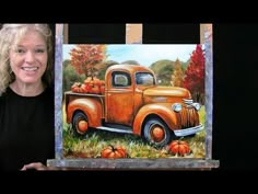 a woman holding up a painting of an orange truck with pumpkins on the bed