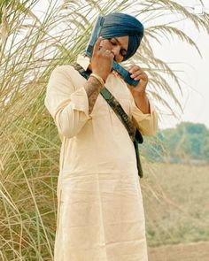 a man with a turban talking on a cell phone while standing in front of some tall grass