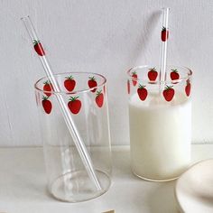 two strawberries on the side of a glass next to a bottle of milk and spoons