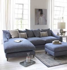 a living room with blue couches and pillows on the bottom right hand corner, next to a large window