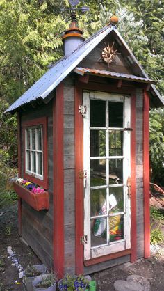 a small red and white shed with a window on the side, potted plants outside