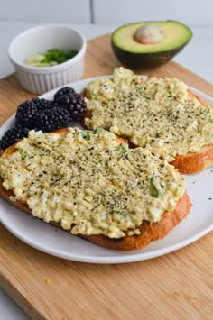 two pieces of bread on a plate with berries and avocado