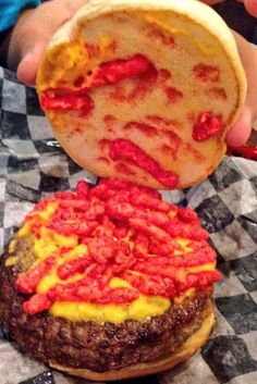 a hamburger covered in red sauce sitting on top of a checkered table cloth next to a person's hand