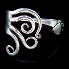 a silver ring with swirly designs on the front and back sides, against a black background