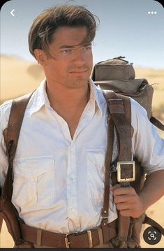 a man in white shirt and brown suspenders carrying a backpack on his back with desert background