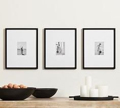 three black and white pictures hang on the wall above a table with bowls, candles and eggs