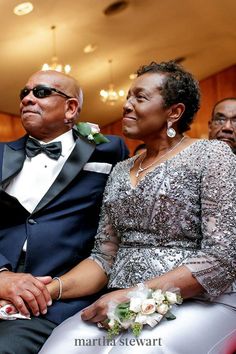 an older man and woman sitting next to each other at a formal event in front of people