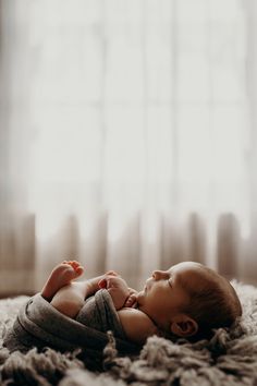 a baby laying on top of a bed next to a window