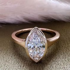 a pear shaped diamond sits on top of a cushioned surface in front of a feather