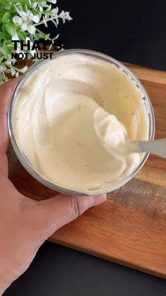 a person is holding a spoon over a bowl of mayonnaise on a cutting board