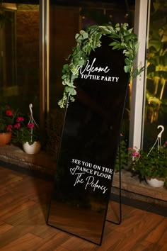 a welcome sign sitting on top of a wooden floor next to potted plants in front of a window