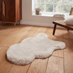 a white sheepskin rug is on the floor in front of a window and chair