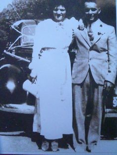 an old black and white photo of two people standing next to each other in front of a car